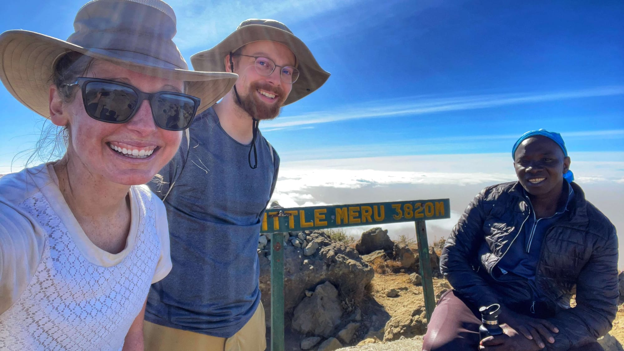 Clara Ritger, and two men take a selfie with a sign that reads, "Little Meru 3820 M."