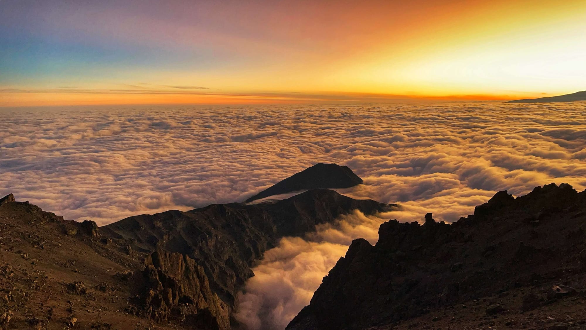 The ridge line of Mount Meru is orange, as are the clouds, at sunrise.