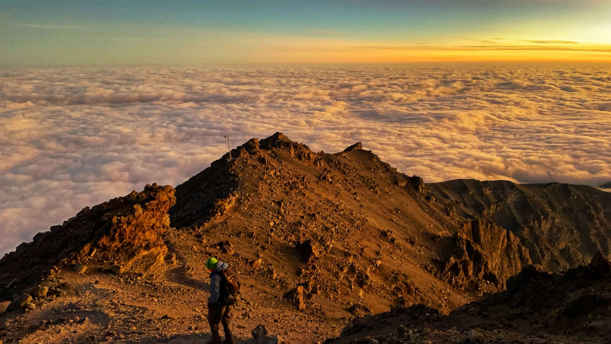 A hiker descends the summit of Mount Meru in its orange, sunrise glow.
