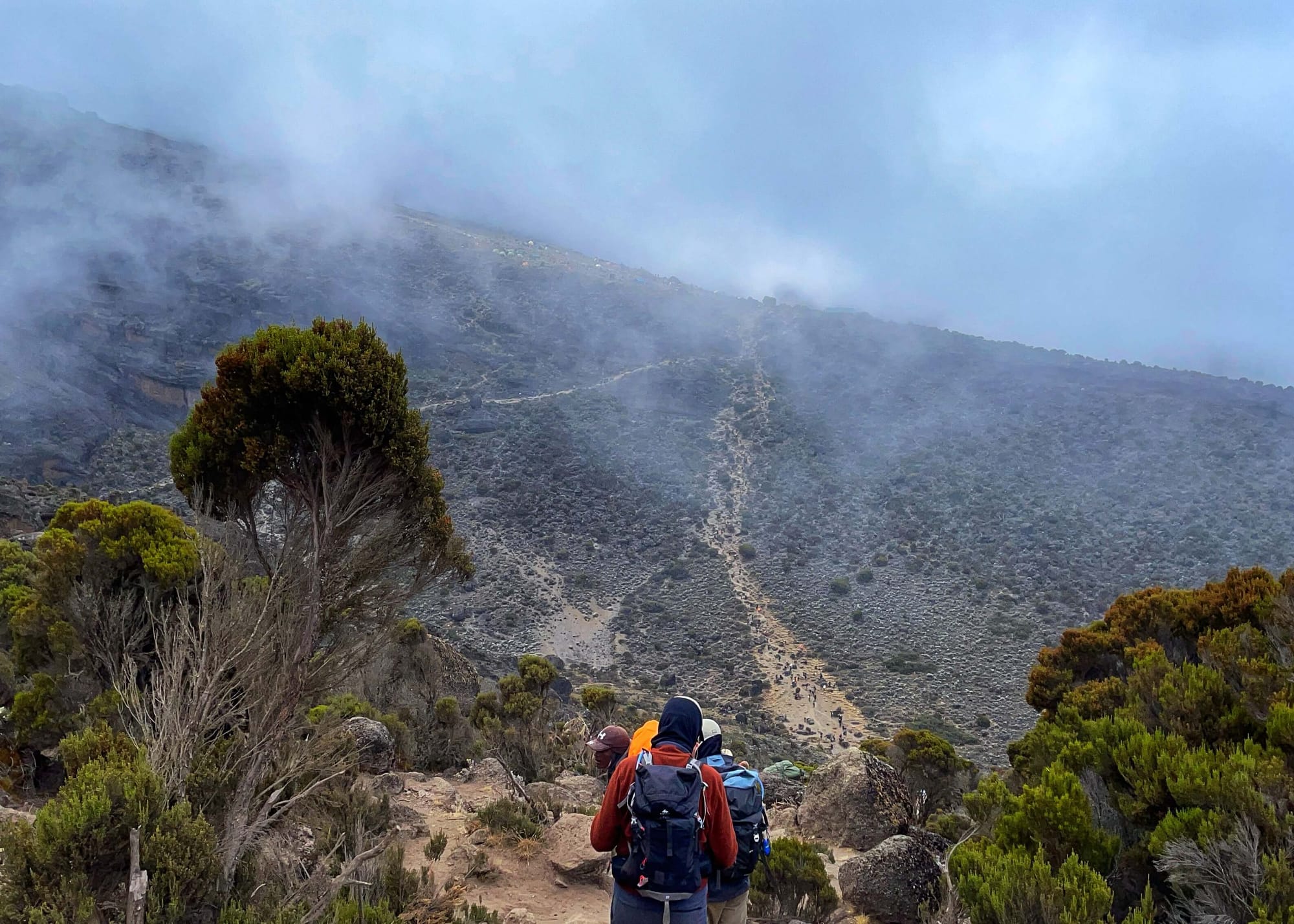 Hikers descend, along a path that can be seen ascending a steep hill ahead.
