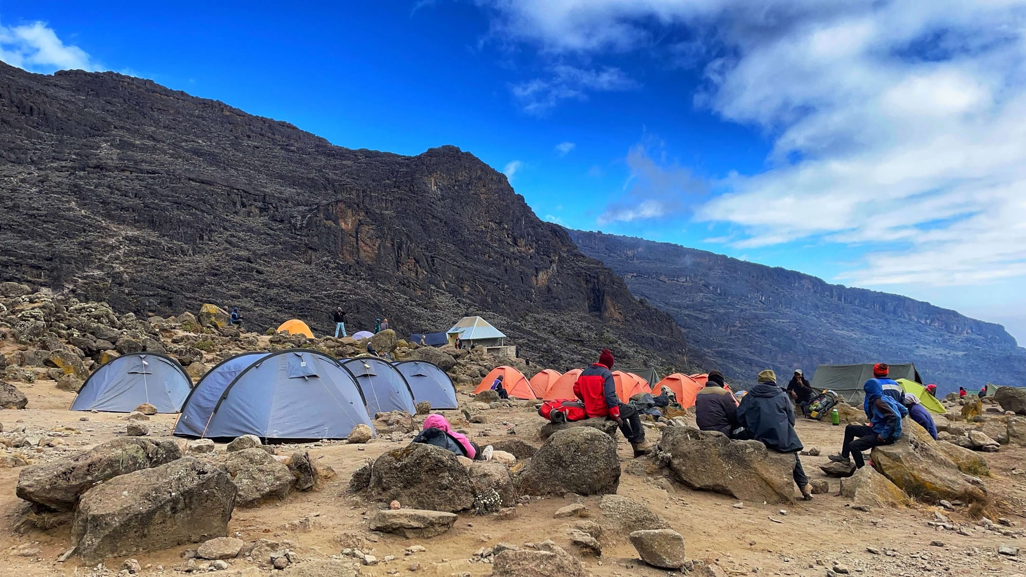 Colorful tents dot the dry dirt landscape, and people sit on boulders.