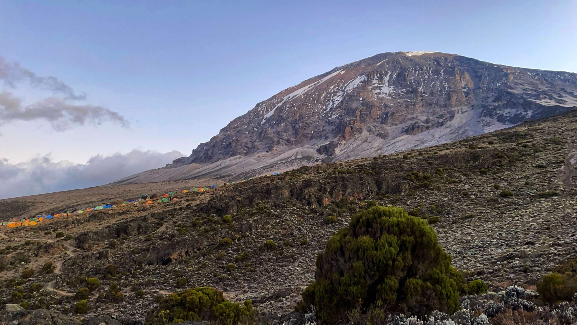 Uhuru Peak at sunrise, with colorful tents dotting the landscape below.