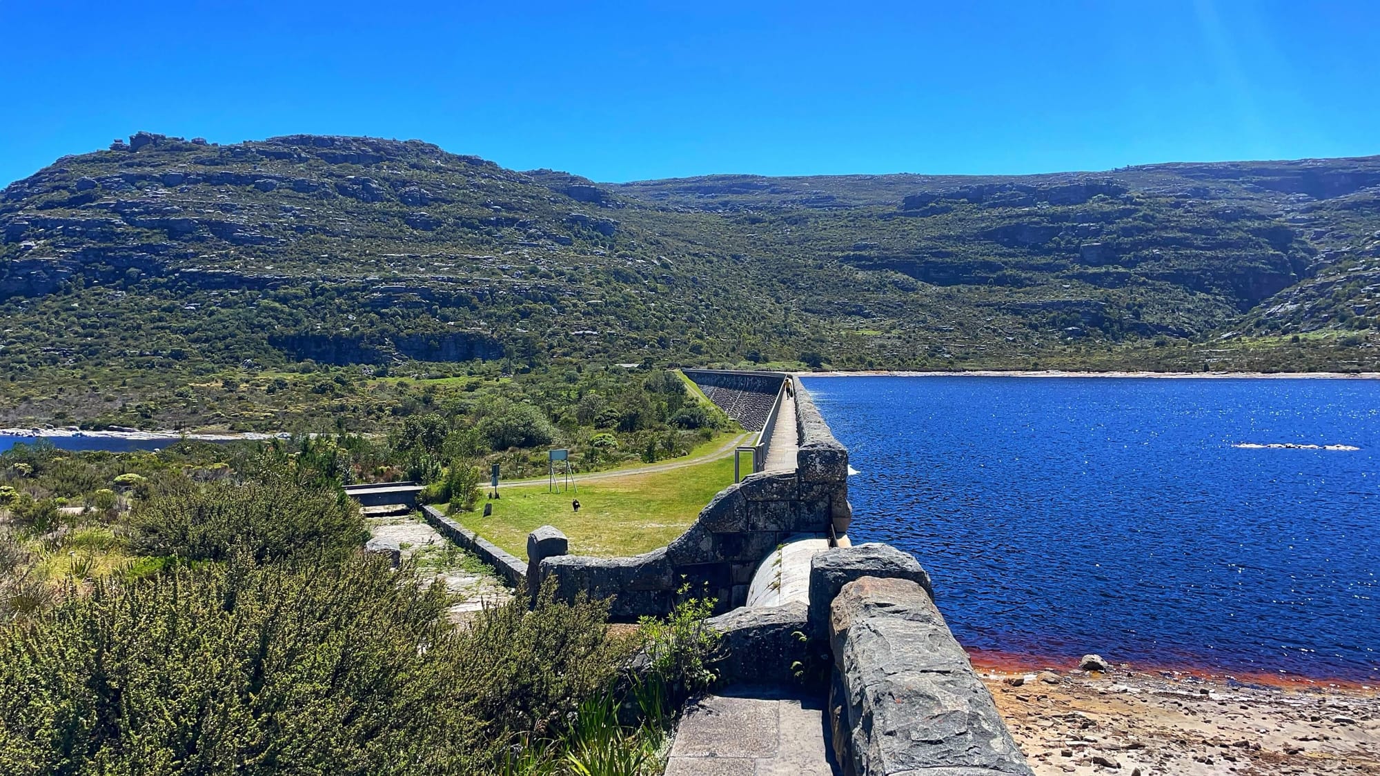 A blue pool above the blue lake, with stone walls like a dam. Hills rise up behind the two bodies of water.