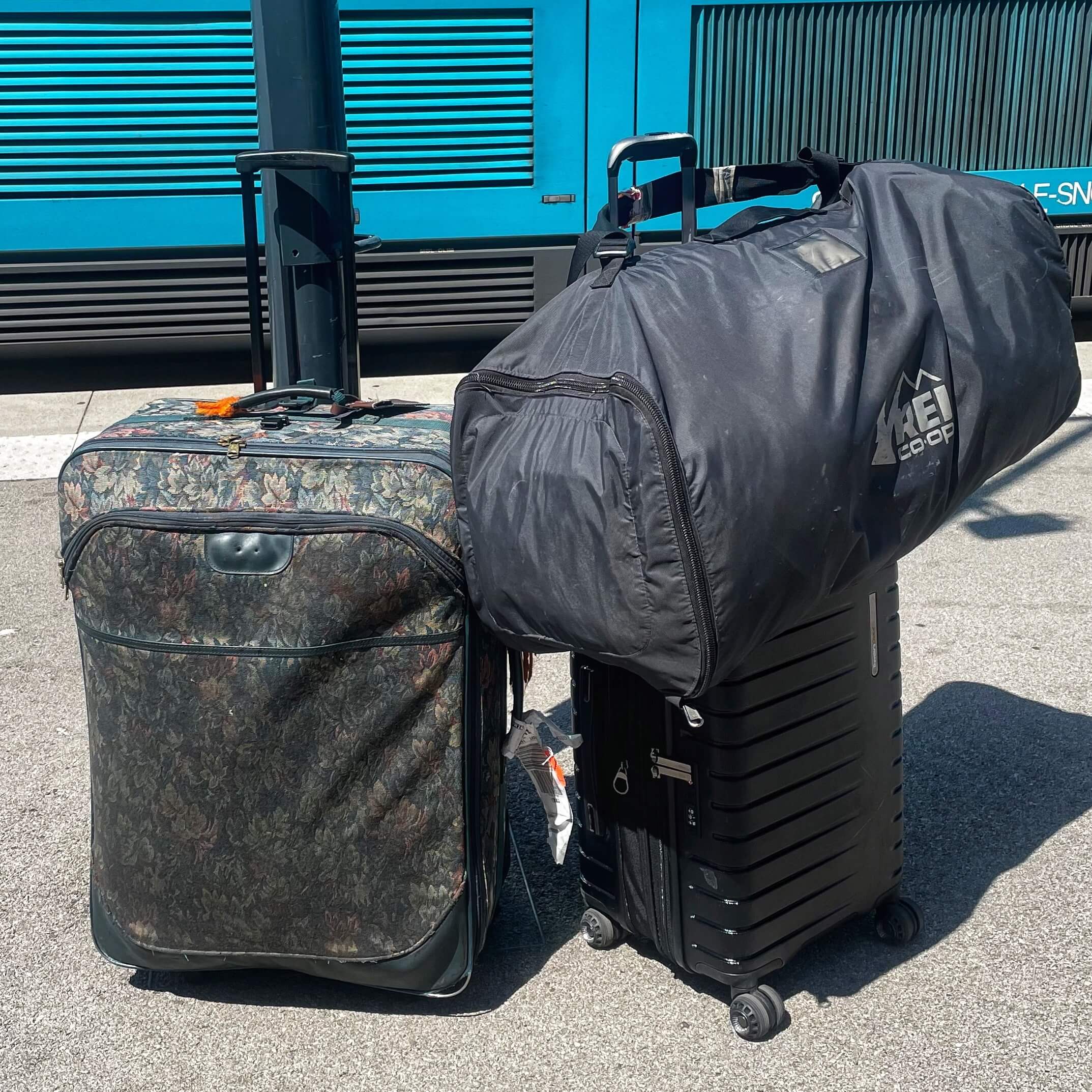 One large floral suitcase next to one small carryon suitcase with one large black duffel bag perched precariously on top.
