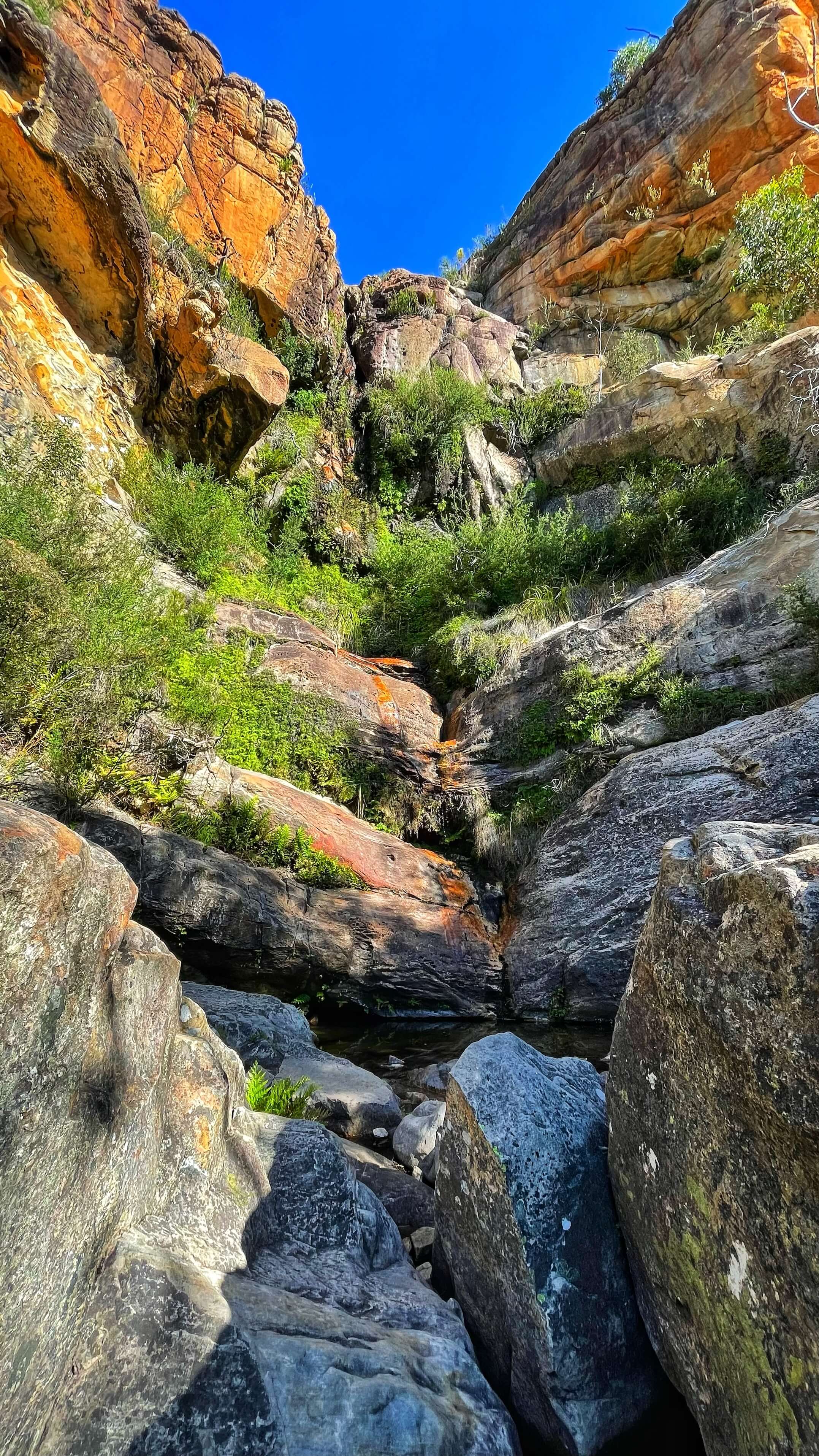 Tall rocks form a horseshoe shape, with big boulders down below. In the middle a waterfall trickles through.