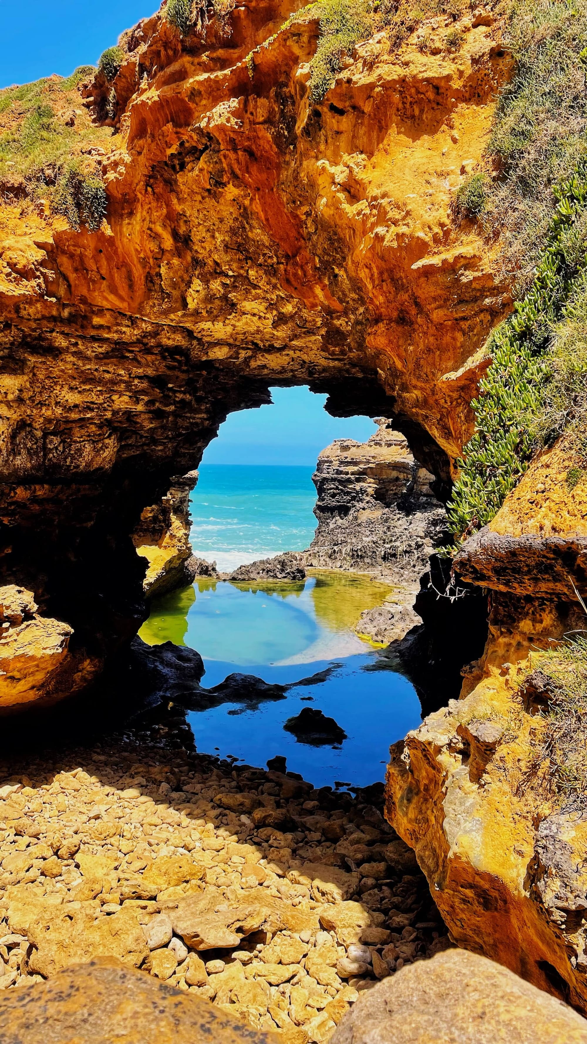 A small pool of water below an arch in the limestone. The ocean peeks out from behind.