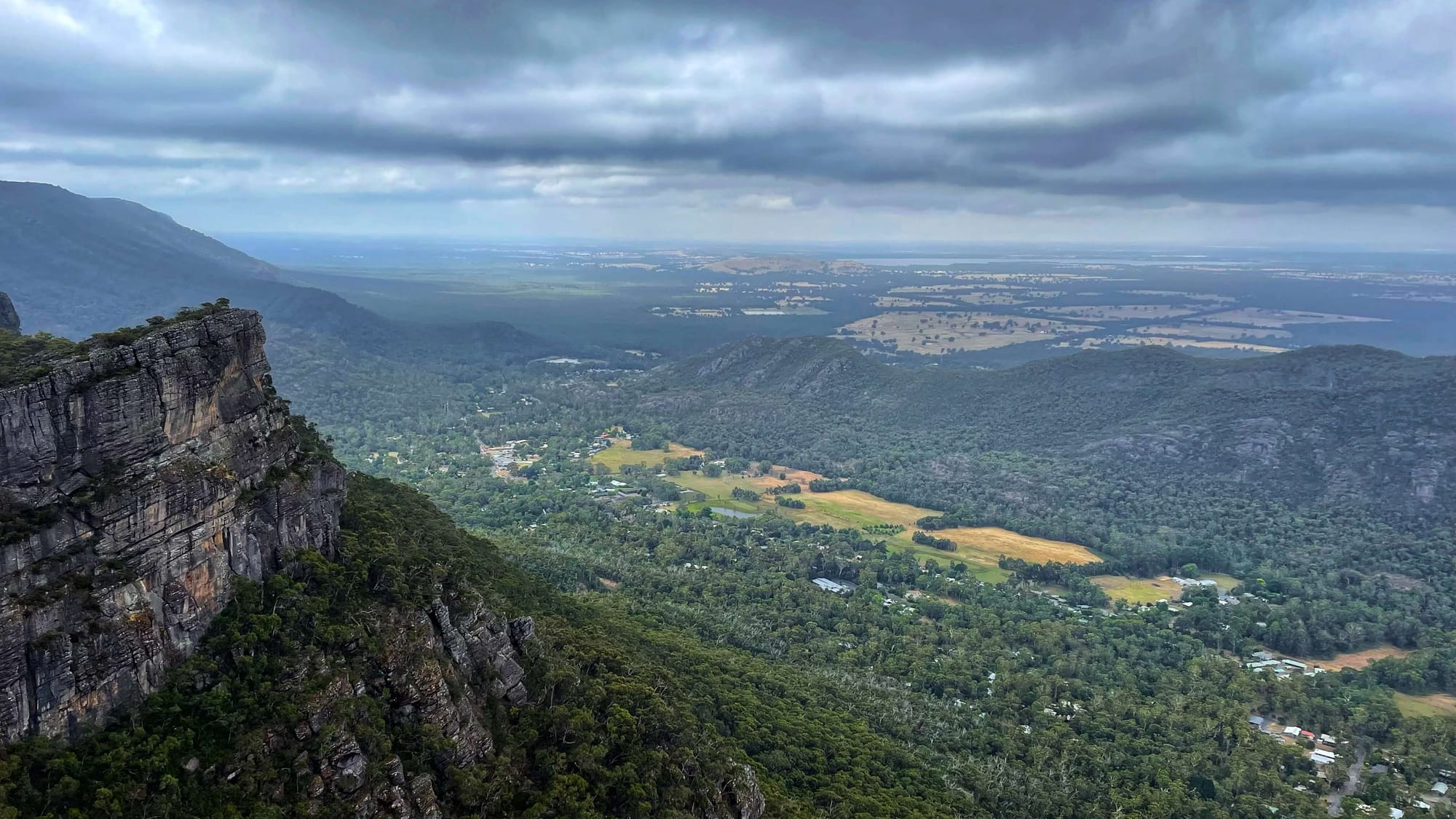 A wide view of a viewpoint, rising up over the valley and town below, filled with trees.