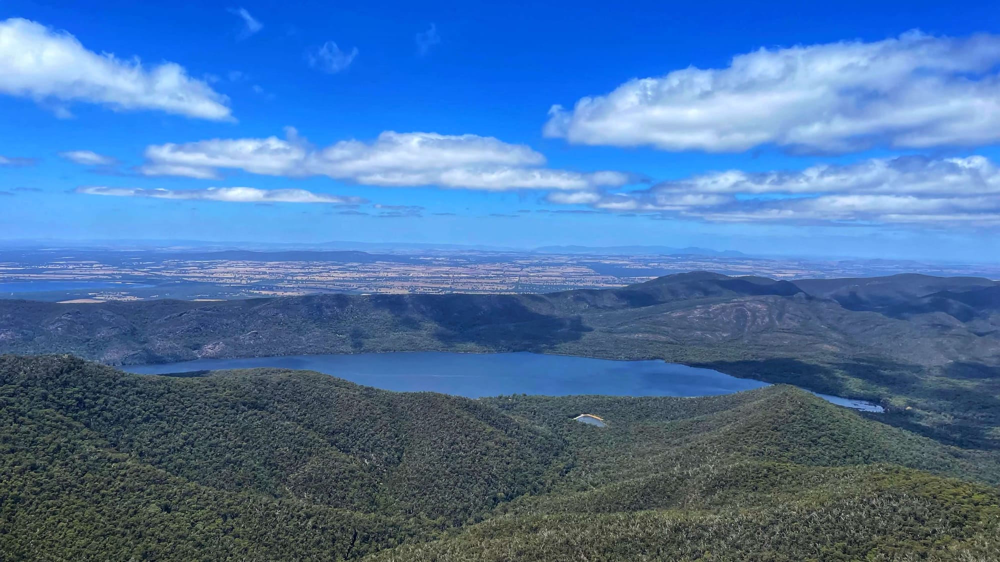 A big blue lake in the distance, in between rolling hills of trees.