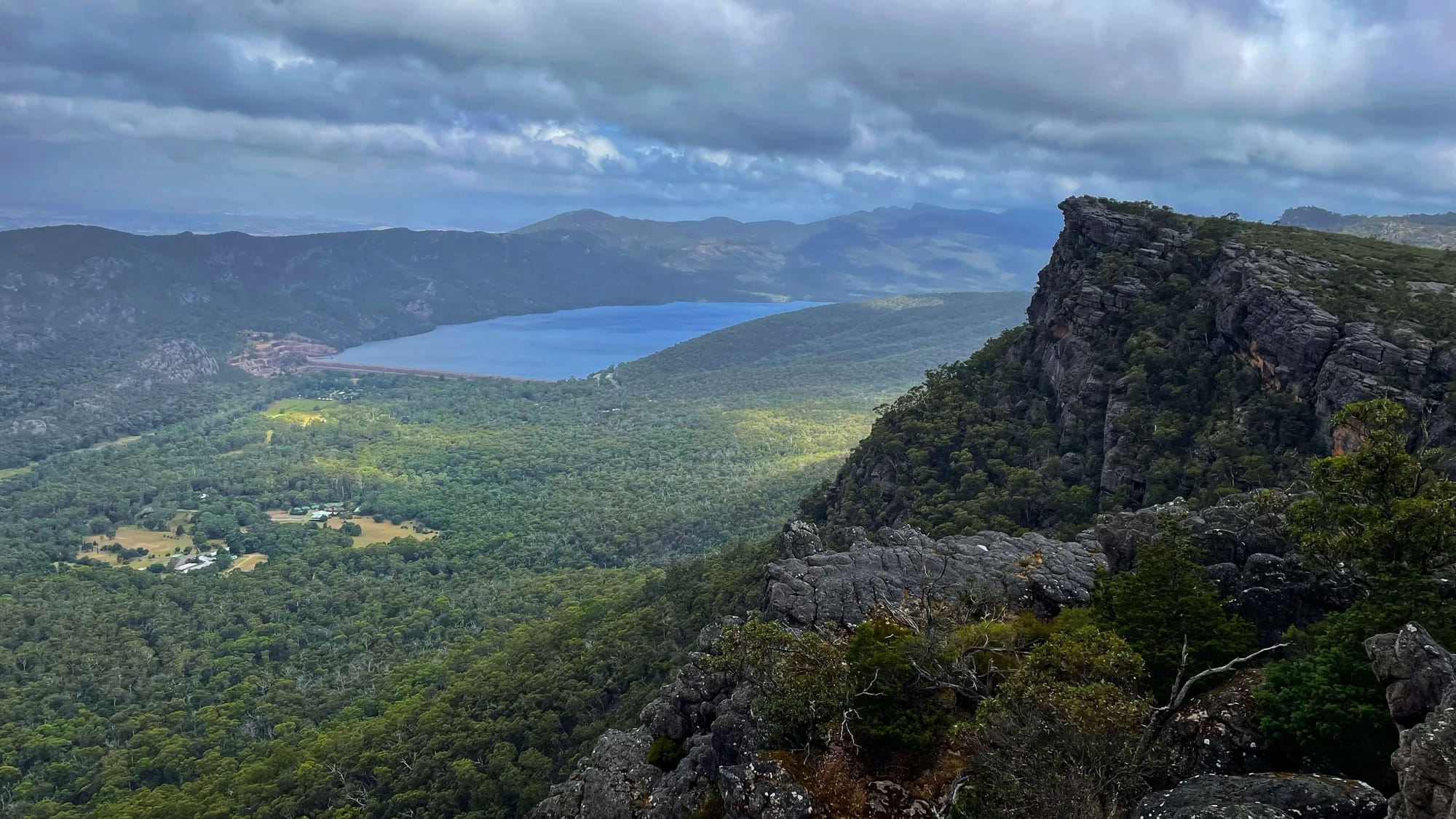 A viewpoint that drops off into a valley of trees, with a big blue lake in the distance.