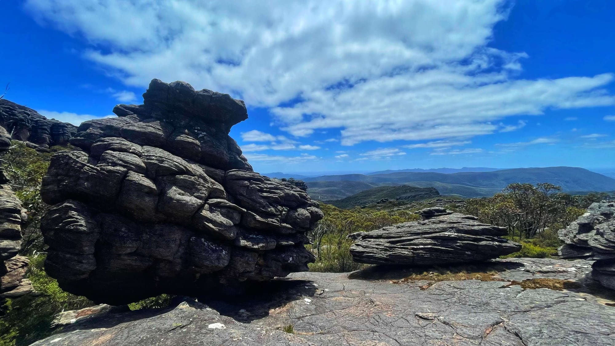 A boulder with knobs and layers of sandstone sits on top of a rocky landing.