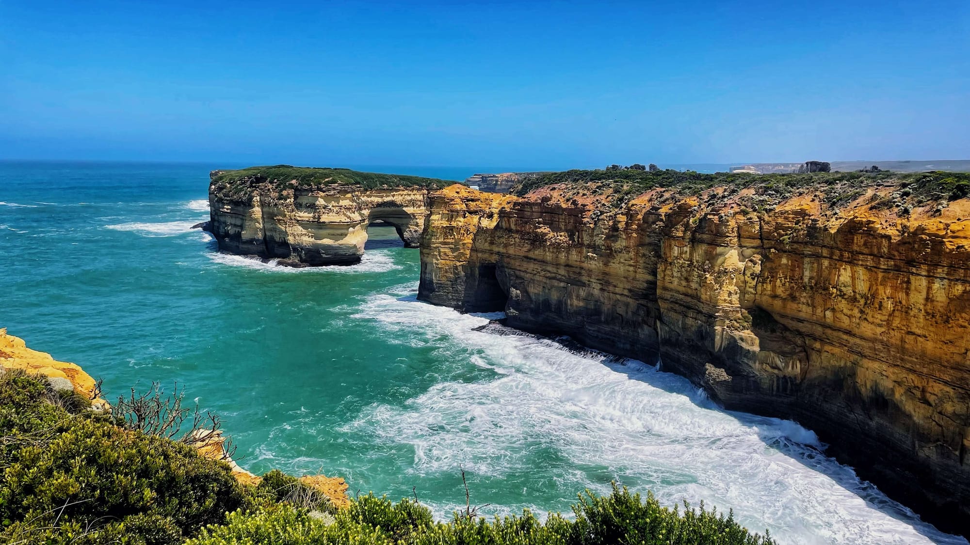 An arch at the base of a limestone rock formation in the ocean. Water passes through.