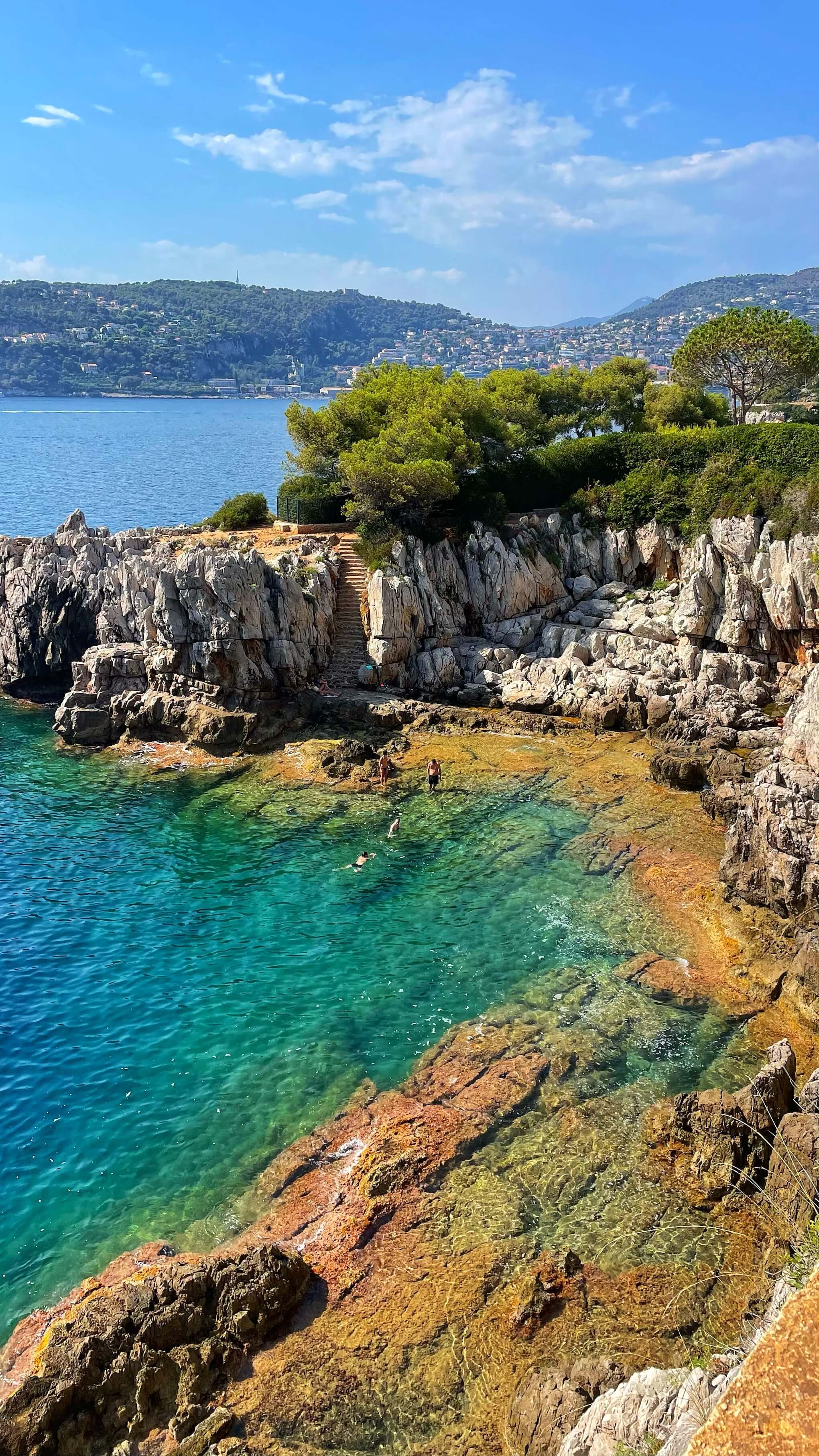 Four people swim along the rocks of Pointe de la Cuisse, an inlet along the Cap Ferrat