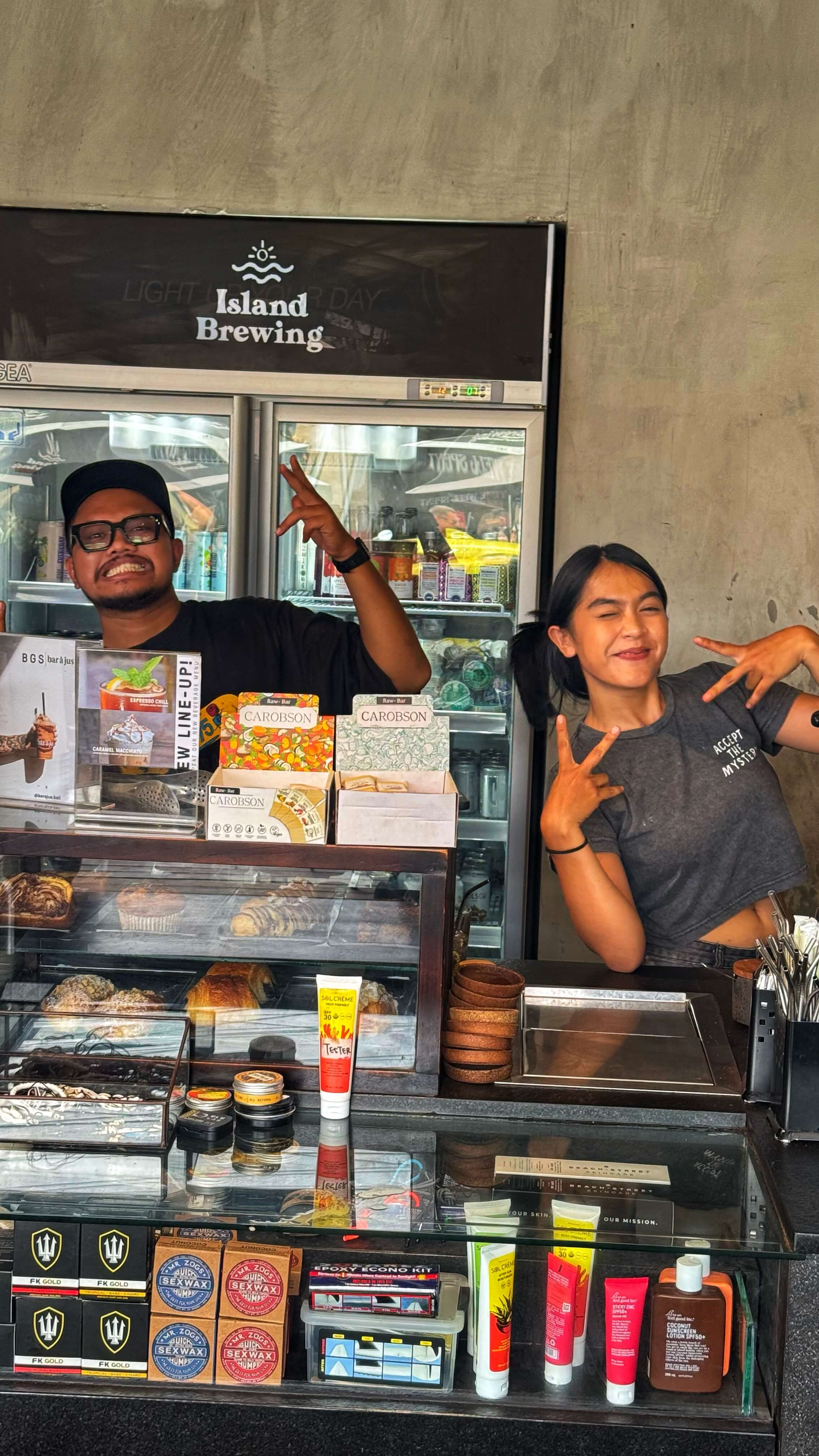 Two employees at a coffee shop make silly faces and pose for a picture.