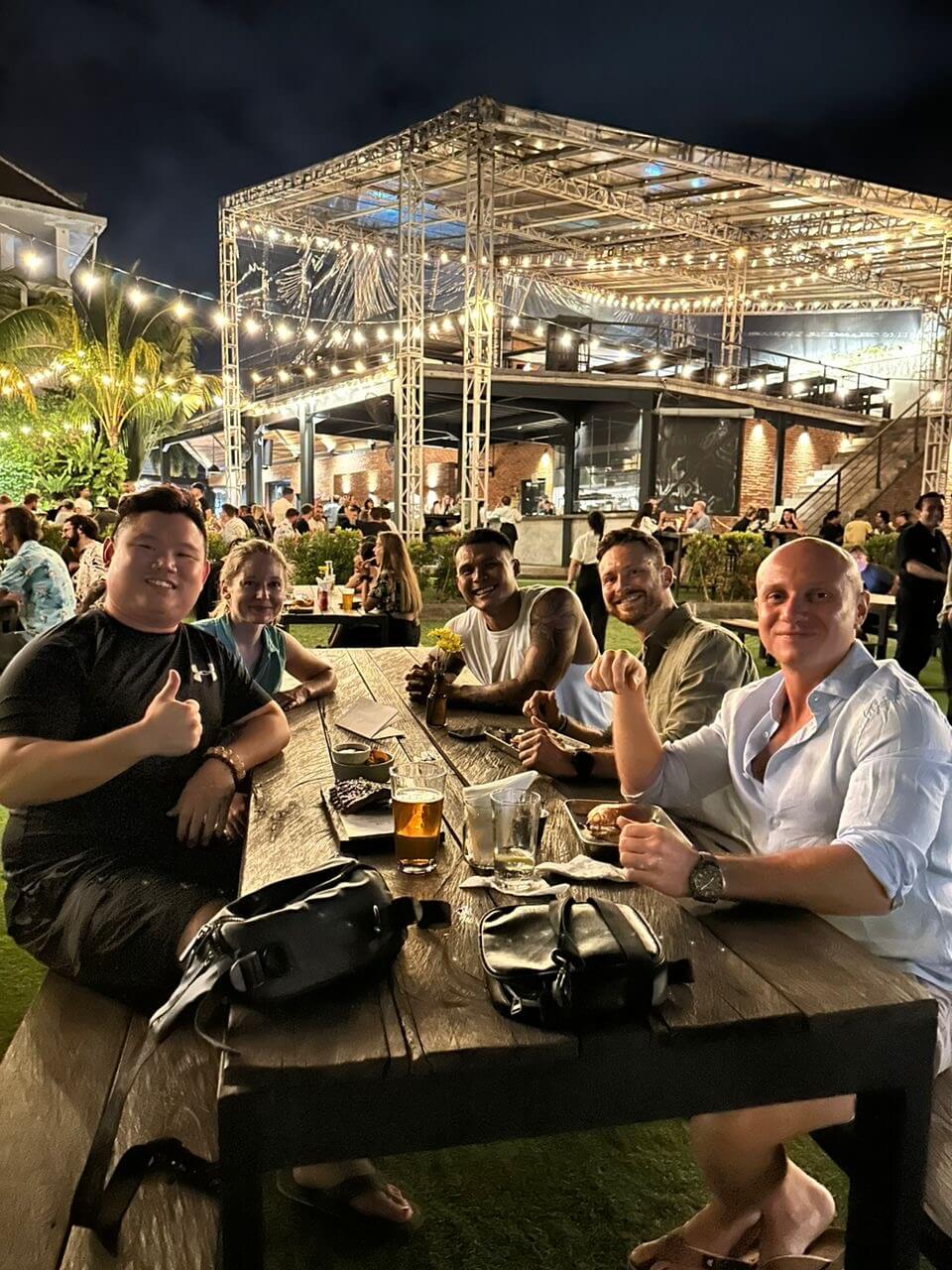 A group of five people pose for a photo at an outdoor beer garden lit up at night.