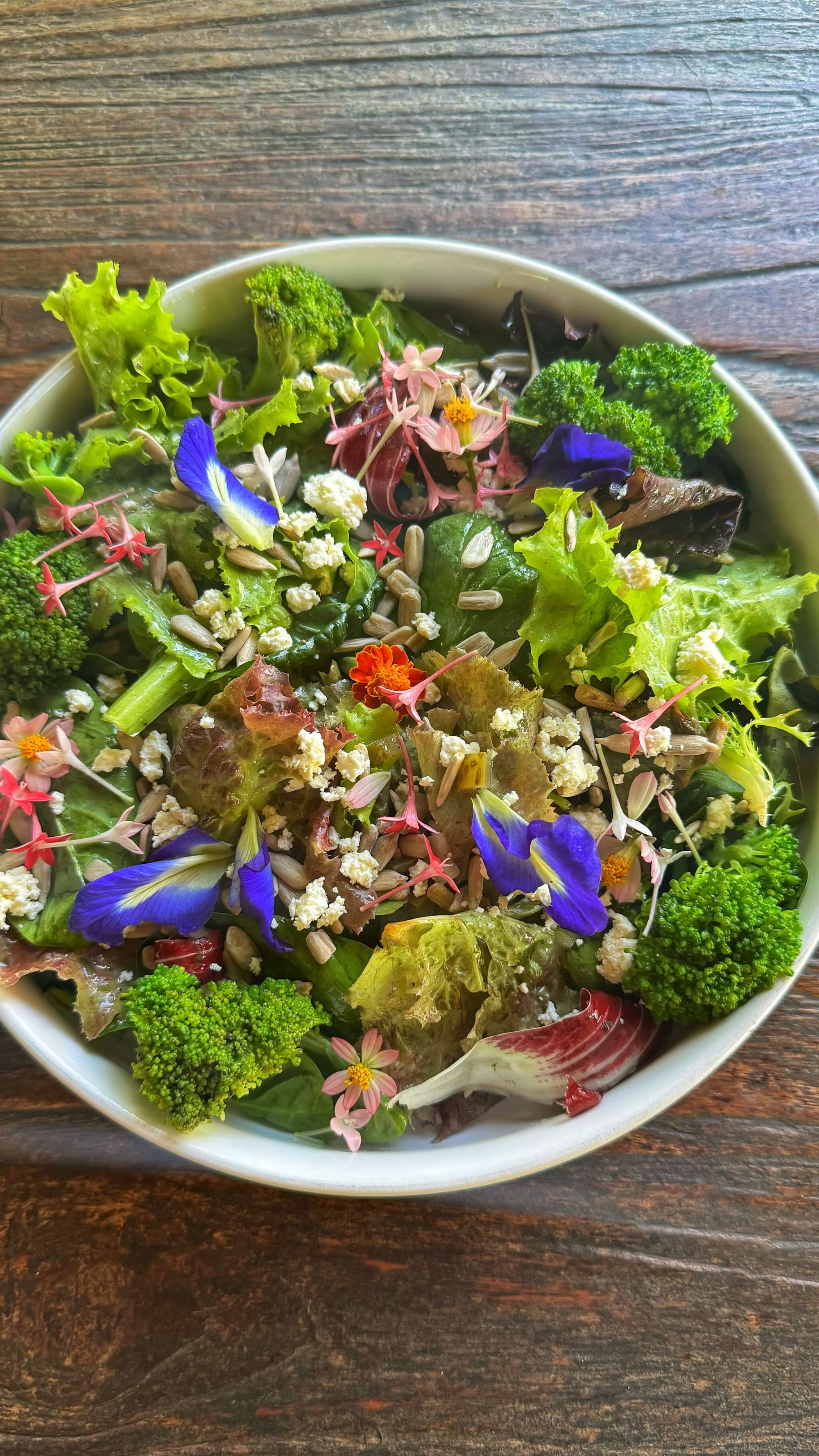 A fresh green salad with broccoli, seeds, and colorful flowers.