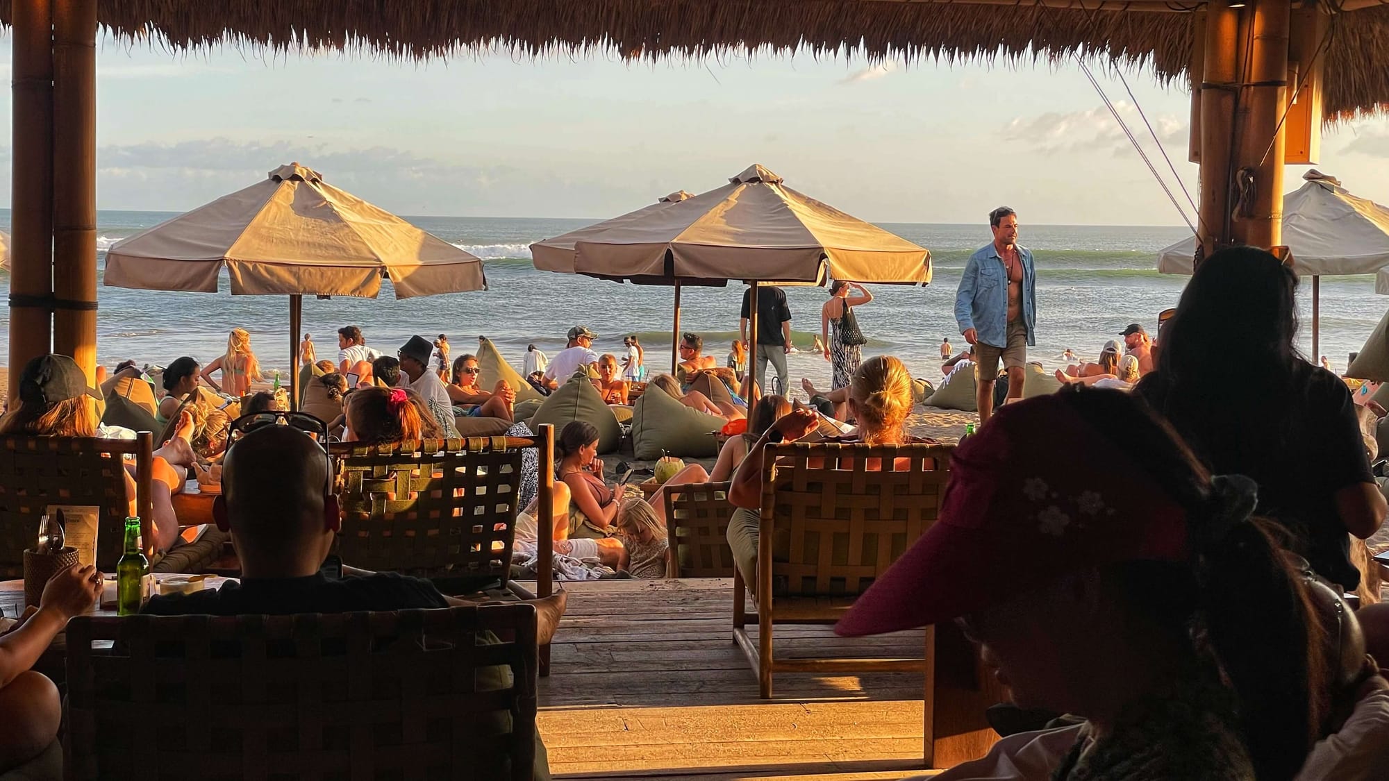 A busy beachside establishment with bean bags and white umbrellas as sunset casts a golden glow.