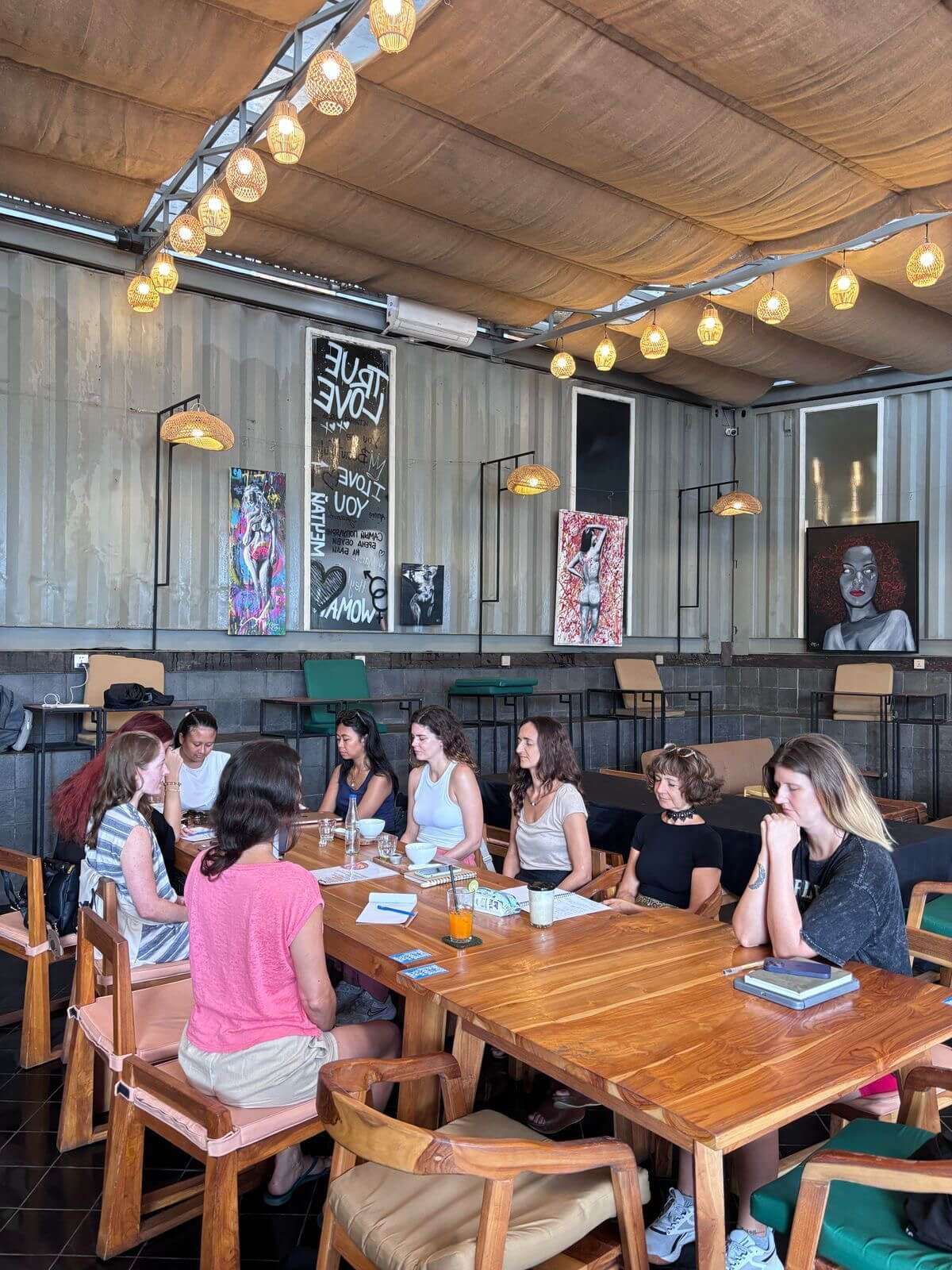 A group of ten women around a cafe table with notebooks and pens. 
