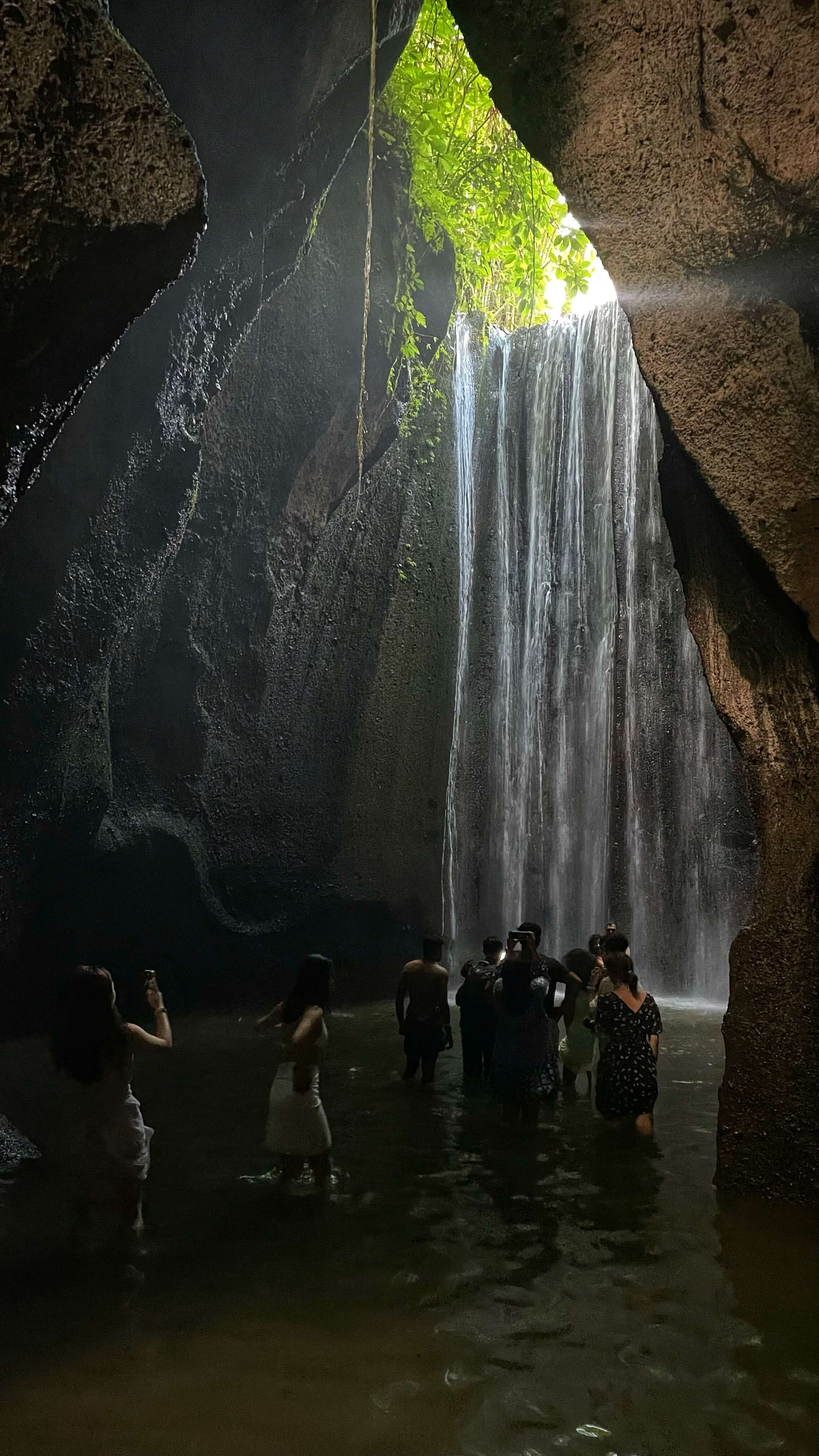 More than a dozen tourists gather in the shadows of a waterfall to take pictures.
