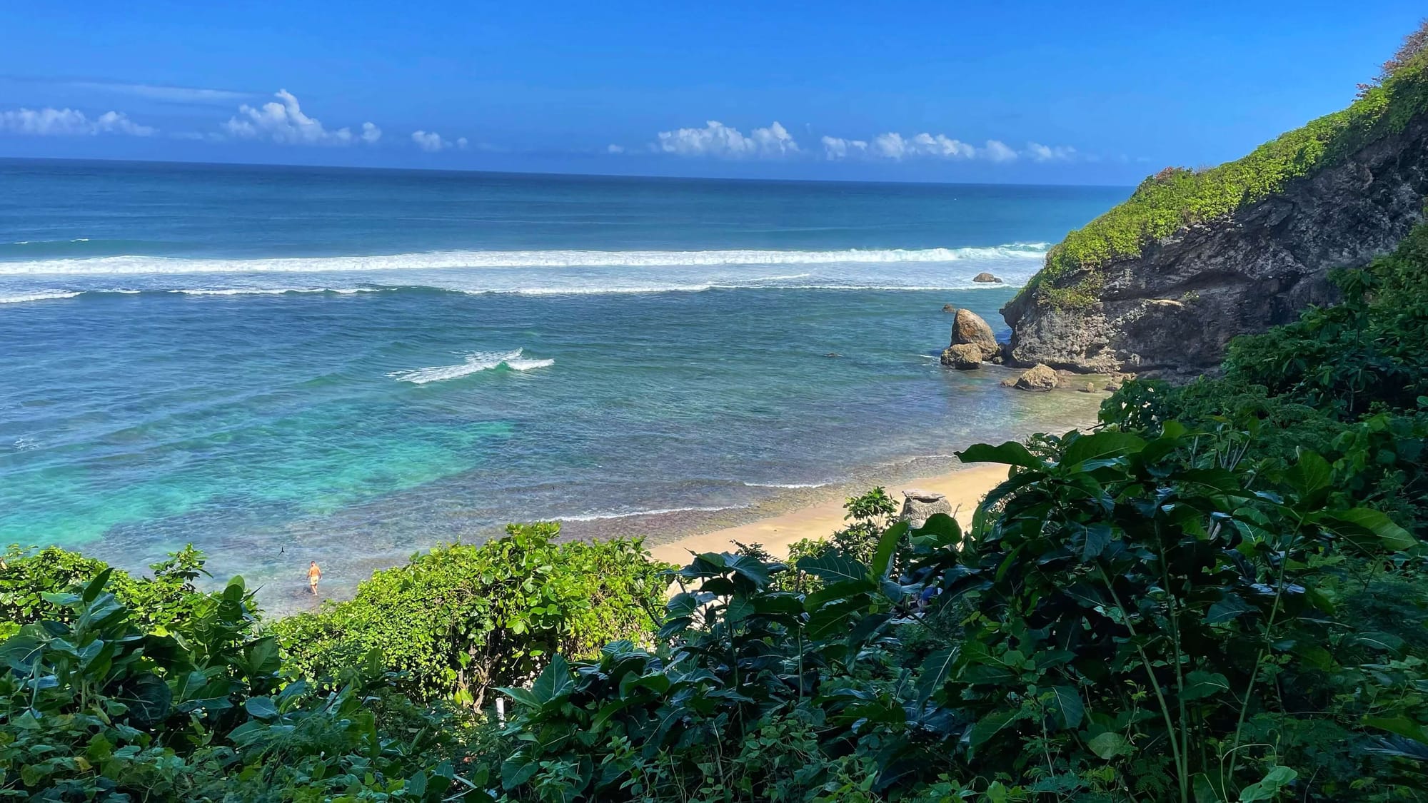 View of a sandy beach with clear blue water from a cliffside.