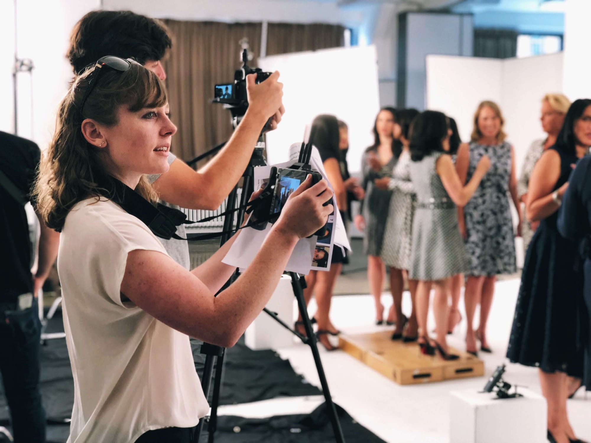 Clara Ritger holds a director's monitor mid-shoot with female corporate executives.