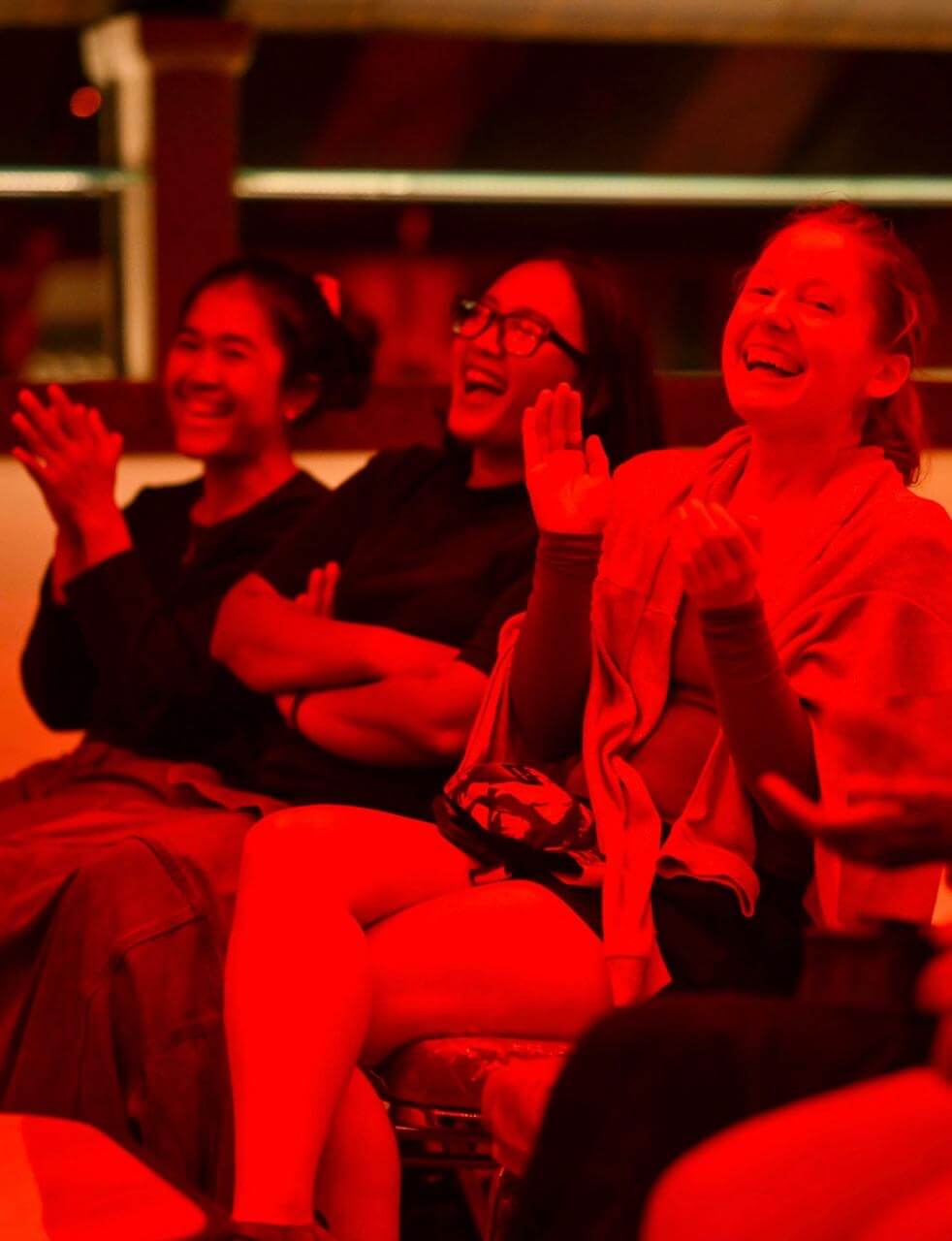 Clara and two Indonesian girls laughing and clapping in the audience of a red light club.