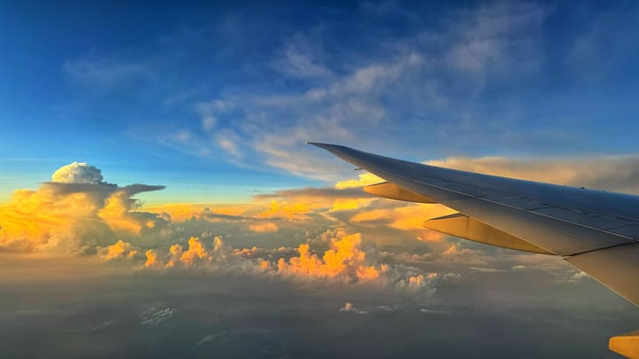 View of sunrise from an airplane window seat. Orange and yellow colored clouds and blue sky.