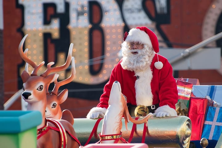 Santa in a parade, riding a sleigh pulled by plastic reindeer.