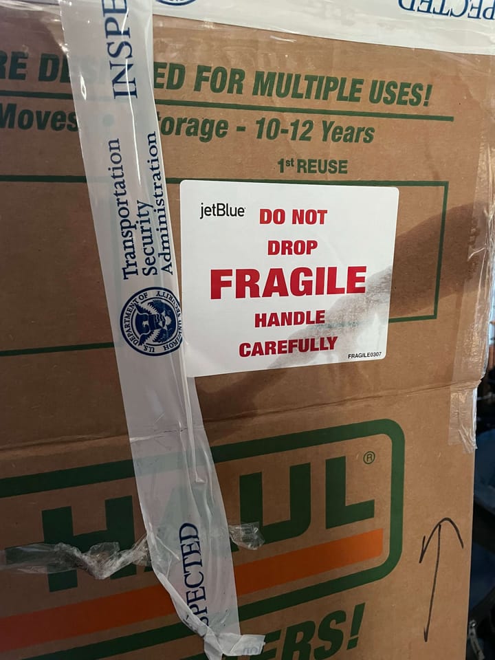 A moving box with a fragile sticker and a TSA inspected ribbon of tape.