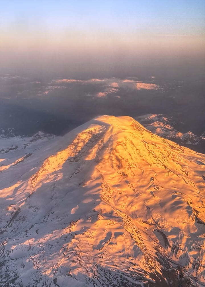 Pink sunlight hits the side of Mount Rainier, Washington, viewed from above.