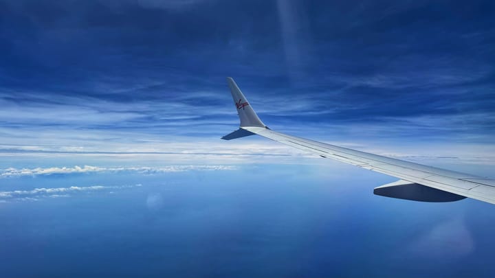 Window view of a Virgin airplane flying through a blue sky.