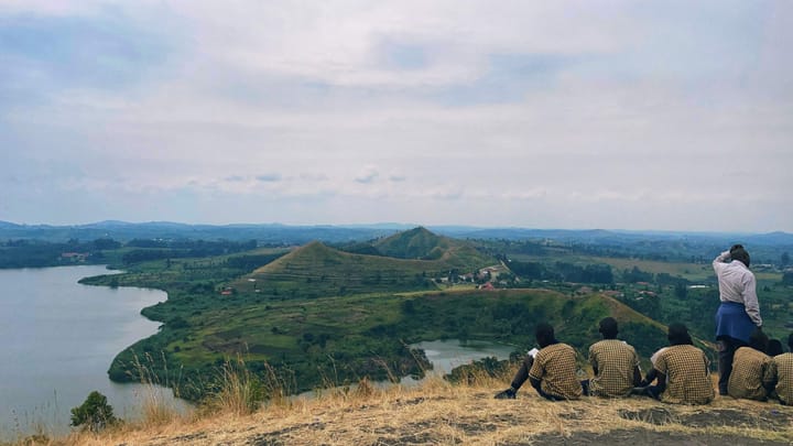 Five youth in matching uniforms facing a viewpoint with hills and a lake. A teacher is talking.
