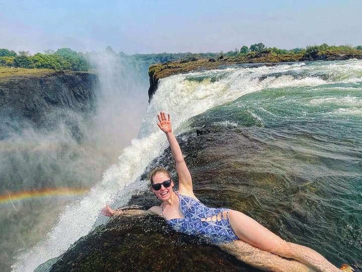 Clara Ritger leans over the edge of Victoria Falls with her hands in the air. 