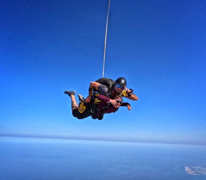 Clara Ritger gives a thumbs up and her instructor salutes the camera while tandem skydiving in Dubai.