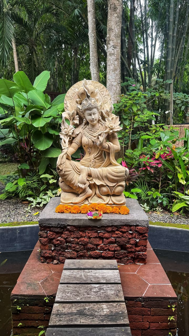 A statue with marigolds and an offering, surrounded by lush tropical jungle. 