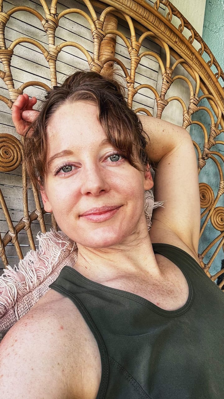Clara Ritger looks at the camera with an easy, relaxed expression. She sits upright, with her head resting against her arm. 