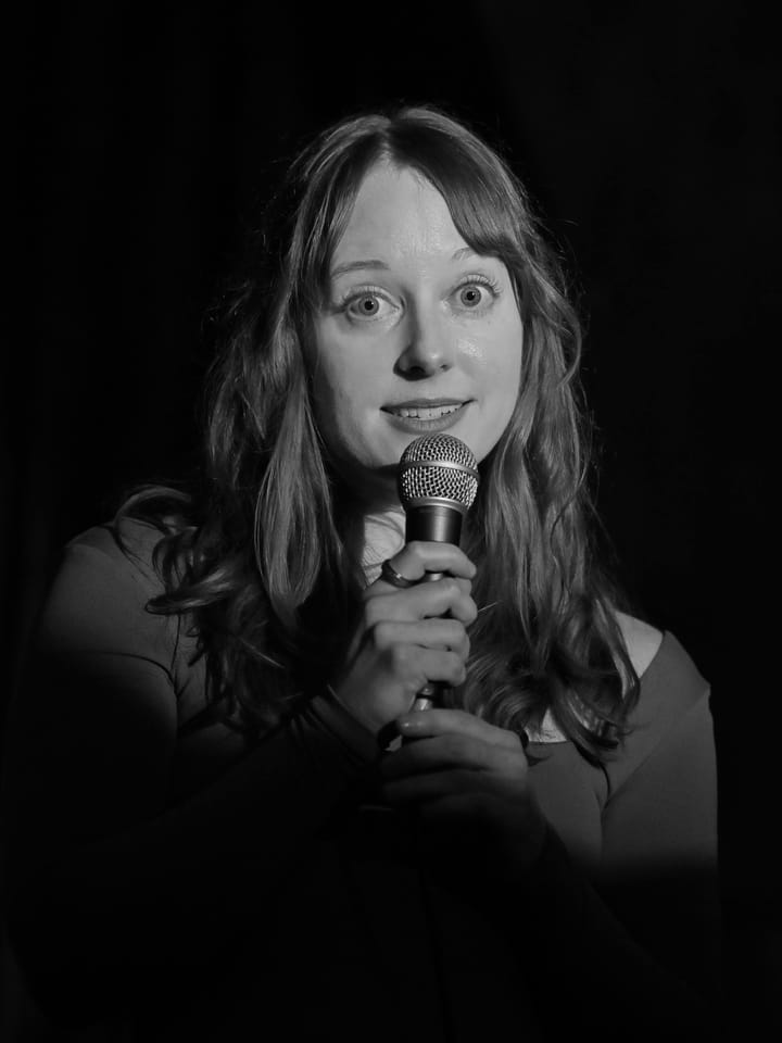 Clara Ritger, in a black and white photo, holds a microphone and looks a little guilty. 